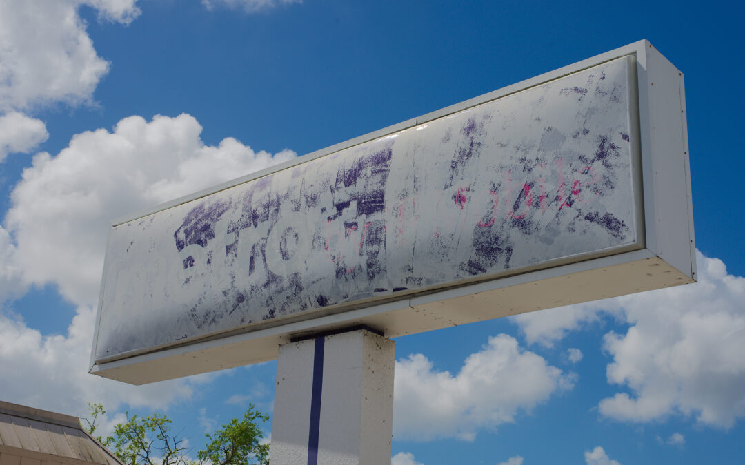 Faded outdoor billboard with worn, barely visible text showing outdated advertising