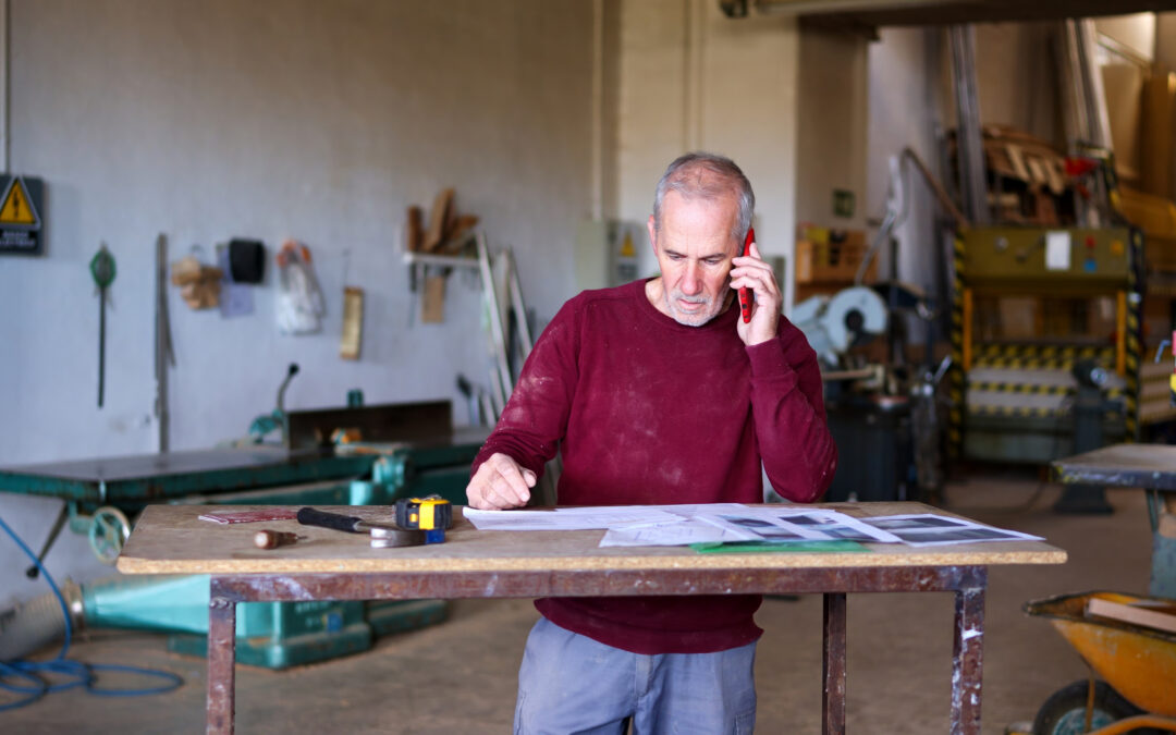 Small business owner reviewing plans while speaking on the phone in his workshop